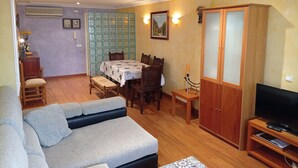 Ein Wohnzimmer mit einer Couch, einem Esstisch mit Stühlen, einer TV-Bank und einem Schrank.