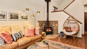 Una sala de estar acogedora con una chimenea de piedra, un sofá con cojines estampados, un sillón colgante y cuadros enmarcados en la pared.