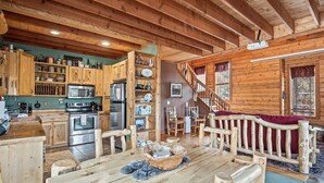 Interior de una cabaña de madera con cocina, comedor y escalera.