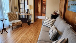 Ein Wohnzimmer mit einer Couch, einem Sessel, Holzboden und einer Tür zu einem anderen Raum.