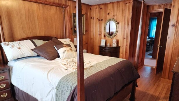 Ein Schlafzimmer mit Holzvertäfelung, einem Himmelbett, einem Schminktisch, einem Nachttisch, einem Spiegel und einer Tür zu einem anderen Raum.