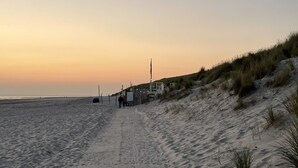 A sandy beach path leading to a dune area with a fence and a signpost.