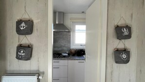 A narrow hallway leading to a kitchen with wooden walls, a white radiator, and hanging decorative bags.