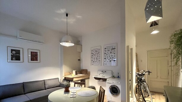 A compact living space with a dining area, a sofa, a washing machine, and a bicycle. - Old Town Apartment (Cēsis)