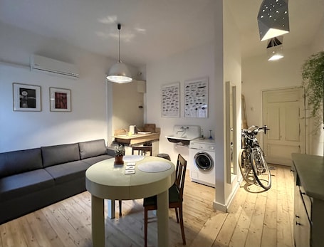 A compact living space with a dining area, a sofa, a washing machine, and a bicycle.