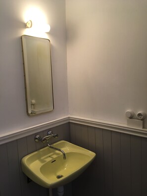 A bathroom with a yellow sink, a mirror, and a wall-mounted light fixture. - Old Town Apartment (Cēsis)