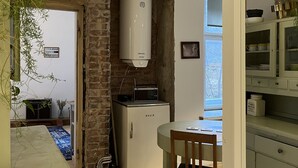 A compact kitchen with a Bosch refrigerator, a microwave, and a water heater. A dining table with a chair is positioned near the kitchen. - Old Town Apartment (Cēsis)