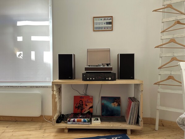 A room with a wooden shelf displaying books, a turntable, and speakers. - Old Town Apartment (Cēsis)
