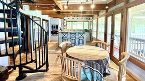 A spacious kitchen with wooden cabinets, a central island with bar stools, and a dining table with a striped tablecloth. - Temple Tree Retreat: An Adventurer's Oceanfront Paradise! (Keaau)