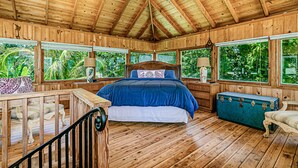A wooden cabin bedroom with a bed, windows, and a chest of drawers. - Temple Tree Retreat: An Adventurer's Oceanfront Paradise! (Keaau)