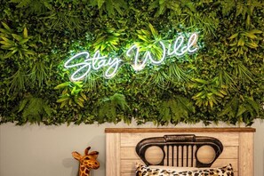 Ein Zimmer mit einem Neon-Schild, auf dem 'Stay Wild' steht, oberhalb einer Wand, die dicht mit Grünpflanzen bewachsen ist.