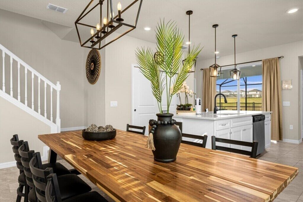 A modern kitchen with a wooden dining table, black chairs, and a large vase with greenery.