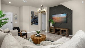 A modern living room with a large sofa, a wooden coffee table, and a television mounted on a dark wall. - 🌺 Aloha Oasis | Private Pool • Windsor Island • Near Disney (Davenport)