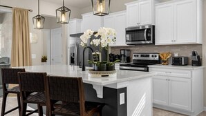 A modern kitchen with white cabinetry, a central island, a built-in microwave, and a stove. - 🌺 Aloha Oasis | Private Pool • Windsor Island • Near Disney (Davenport)