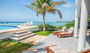 Un espace aménagé au bord de la piscine, avec des chaises longues, un palmier et une vue sur l’océan.
