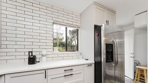 Una cocina moderna con armarios blancos, un refrigerador de acero inoxidable y una ventana con persianas.