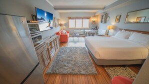 A hotel room with a bed, a desk, a chair, a sofa, a TV, and a refrigerator.