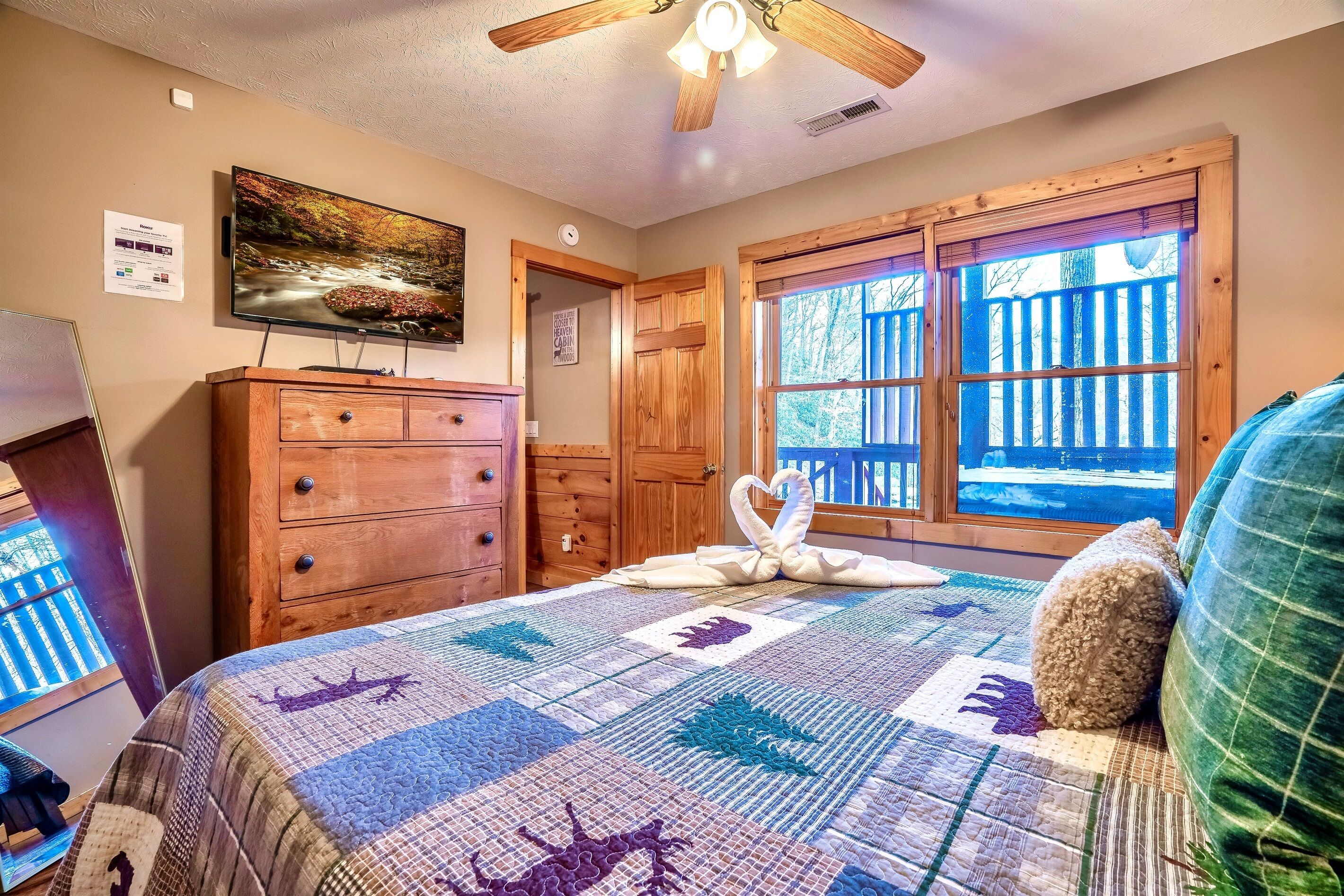 A bedroom with a large bed, wooden dresser, and a television on the wall.
