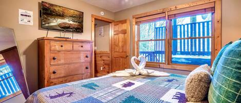 A bedroom with a large bed, wooden dresser, and a television on the wall.