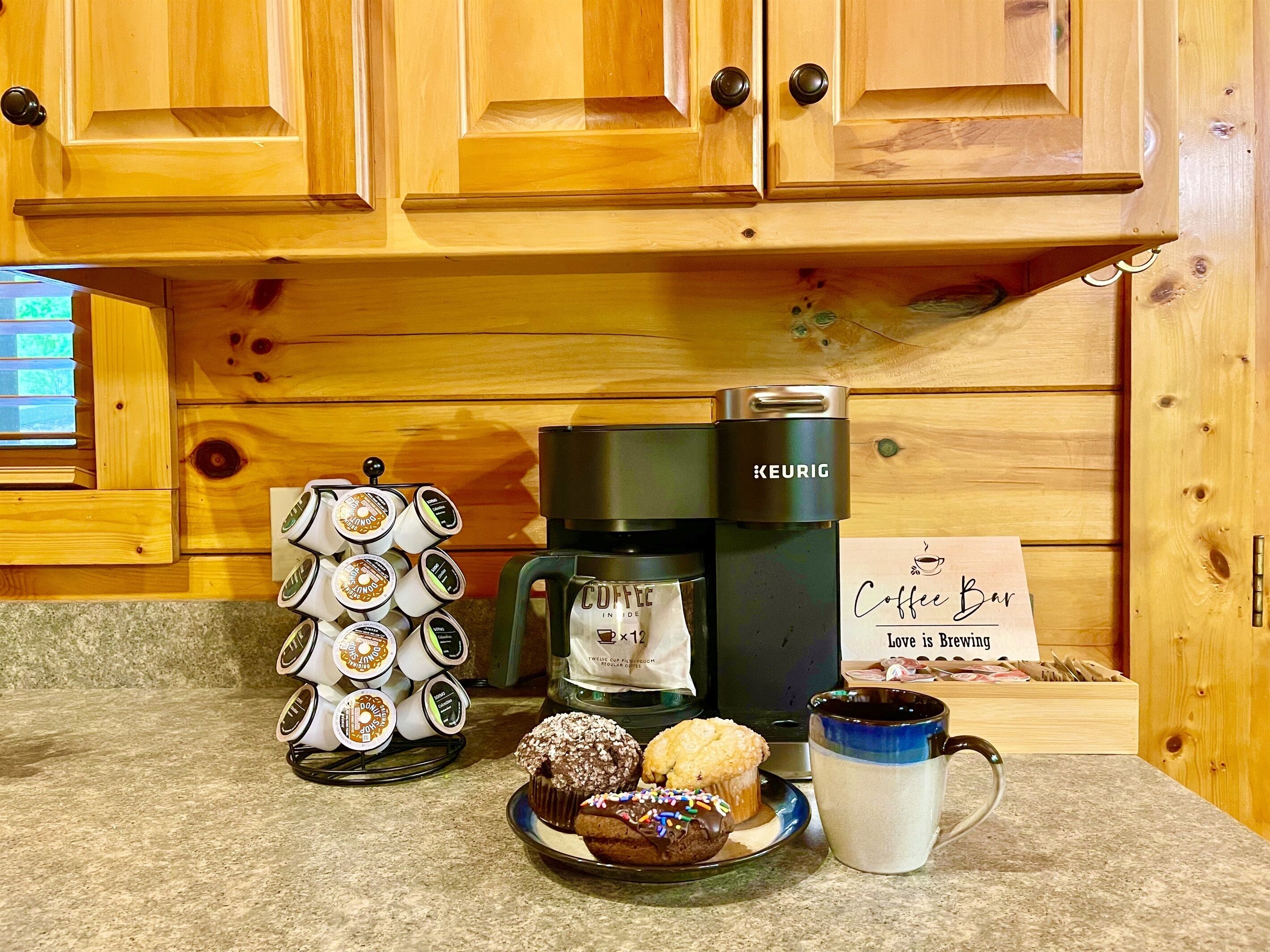 Une machine à café, une tasse et une assiette avec des muffins, le tout posé sur un plan de travail de cuisine.