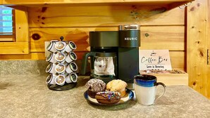 Eine Kaffeemaschine, eine Tasse sowie ein Tablett mit Muffins und einem Cupcake auf einer Küchenarbeitsplatte.