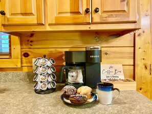 Eine Kaffeemaschine, eine Tasse sowie ein Tablett mit Muffins und einem Cupcake auf einer Küchenarbeitsplatte.