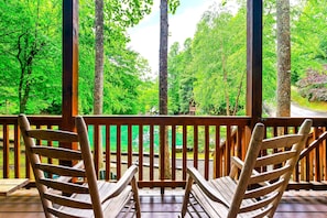 A wooden deck with two rocking chairs overlooking a lush green forest.