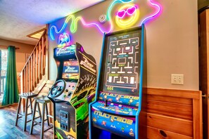 Una stanza con giochi arcade, una scala in legno e un neon.