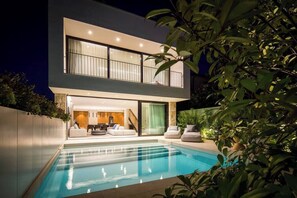 A modern two-story house with a swimming pool, a balcony, and a well-lit interior.