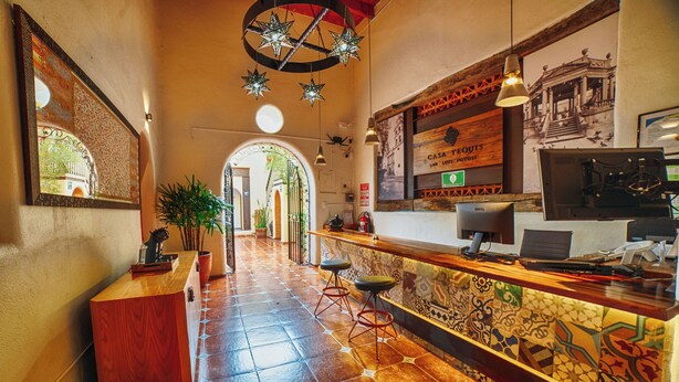 A hotel lobby with a wooden reception desk, a tiled floor, and a large mirror reflecting the entrance. - Hotel Casa Tequis San Luis Potosi (San Luis Potosi)