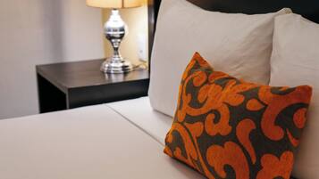 Cama bem arrumada com colchão branco e uma almofada laranja e preta estampada.