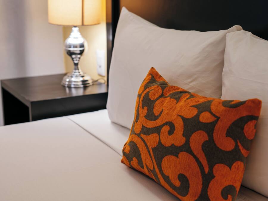 Cama bem arrumada com colchão branco e uma almofada laranja e preta estampada.