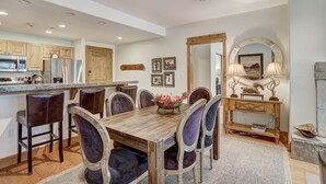 Une cuisine moderne avec des meubles en bois, un réfrigérateur en acier inoxydable et un coin repas comprenant une table en bois et des chaises rembourrées.