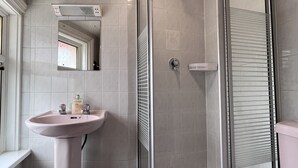 Un baño con lavamanos pedestal, espejo, cabina de ducha y retrete.