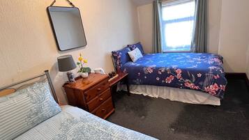 Un dormitorio con cama, una mesita de noche con lámpara, cómoda y espejo en la pared.
