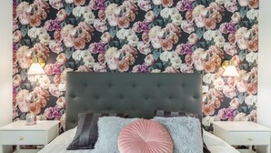 Un dormitorio con papel tapiz floral, cabecero tapizado y lámparas de noche.