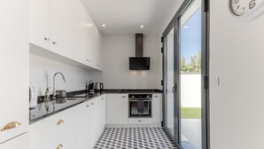 Una cocina moderna con gabinetes blancos, piso a cuadros negro y blanco, horno empotrado y un ventanal con vistas al exterior.