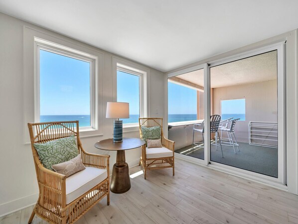 A balcony with wicker chairs, a table with a lamp, and a view of the ocean.