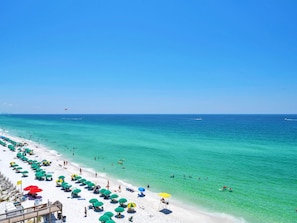 A beach with rows of umbrellas and sun loungers, a wooden walkway, and clear turquoise water.