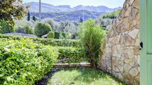 Ein Garten mit Steinmauern, unterschiedlicher Bepflanzung und Blick auf ferne Berge.
