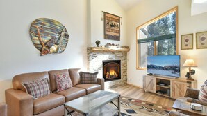 A cozy living room with a fireplace, a large window, and a television. - Chimney Ridge Larkspur Townhome: Hot Tub, Great Location (Breckenridge)