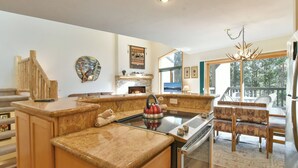 A kitchen with granite countertops, a gas stove, and a built-in oven. There is a dining area with a table and chairs, and a large window offering a view of the outdoors. - Chimney Ridge Larkspur Townhome: Hot Tub, Great Location (Breckenridge)