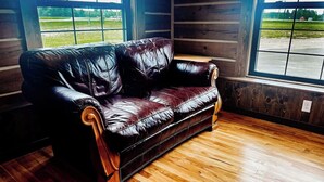 A black leather sofa in a room with wooden flooring and large windows. - {Big Timbers} Lodging next to North Entrance of Itasca State Park (Shevlin)
