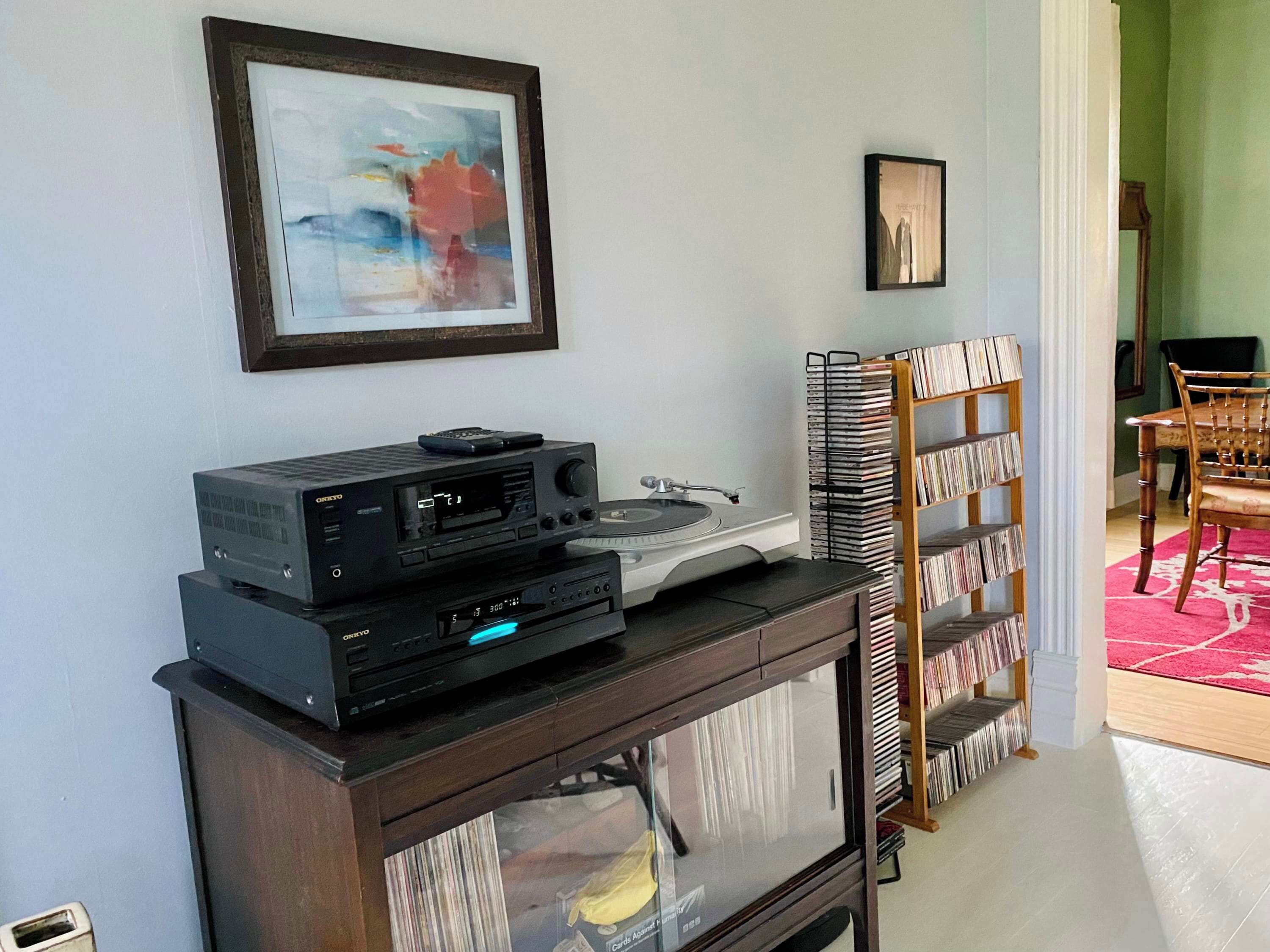 Una sala de estar con televisión, un mueble bajo con reproductor de CD, una estantería y un cuadro enmarcado en la pared.