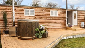 Una cabaña de troncos con terraza de madera, jacuzzi y chimenea.