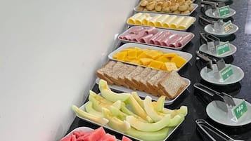 Een buffet met diverse etenswaren, zoals fruit, kazen en vlees.