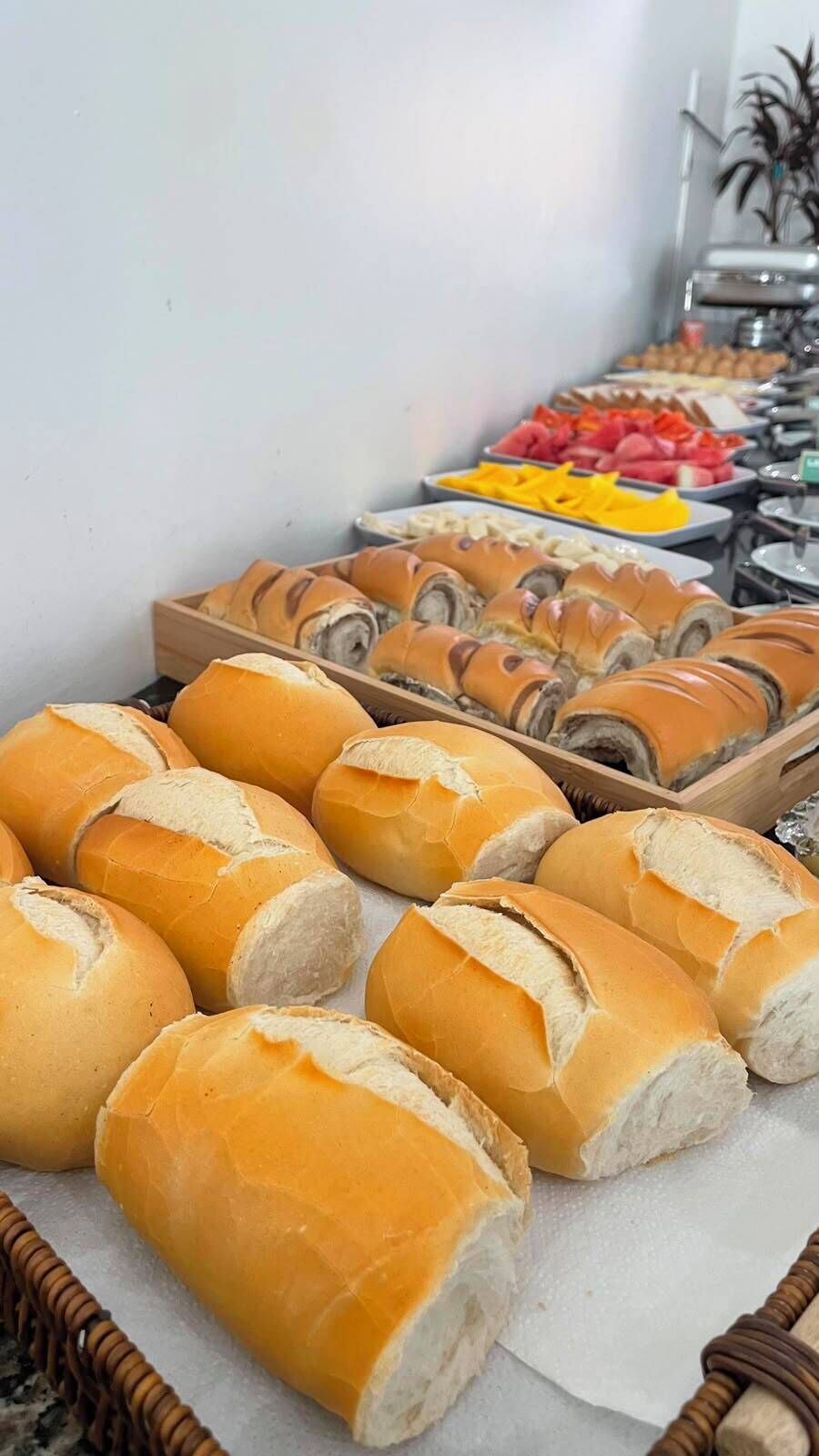 Buffet com diversos alimentos, incluindo pães e frutas fatiadas.