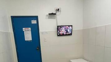 A hotel room with a single bed, a small bedside table, a TV mounted on the wall, and a blue door with a notice.