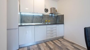 Cozinha compacta com armários brancos, painel de proteção de aço inoxidável e fogão moderno.