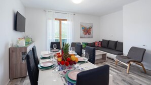 Uma sala de estar moderna com área de jantar, TV de tela plana na parede e uma janela grande com cortinas.